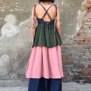 May include: A tiered maxi dress with a dark green top layer, a pink middle layer, and a navy blue bottom layer. The top layer has a navy blue bodice with thin pink and green straps that tie at the back. The dress has a gathered waistline.