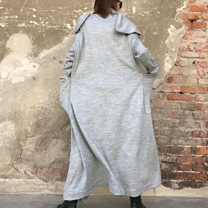 May include: A long, gray, hooded cardigan with large pockets. The cardigan is made of a soft, textured fabric and has a relaxed fit.