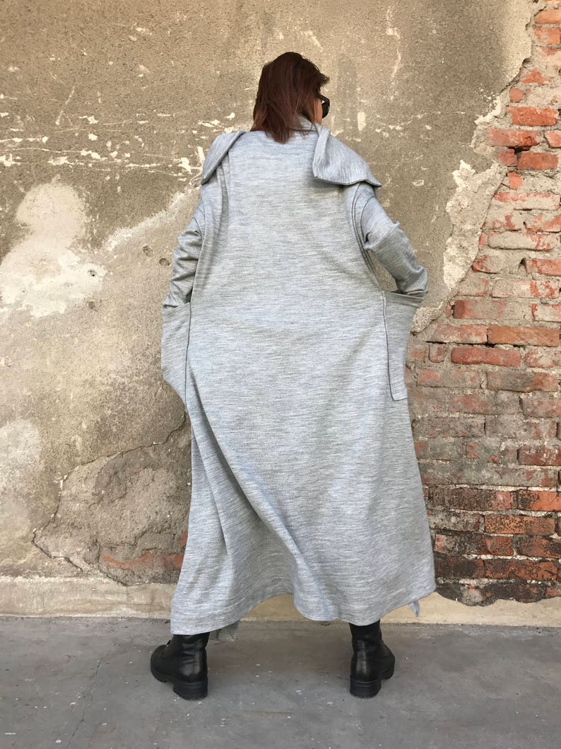 May include: A long, gray, hooded cardigan with large pockets. The cardigan is made of a soft, textured fabric and has a relaxed fit.