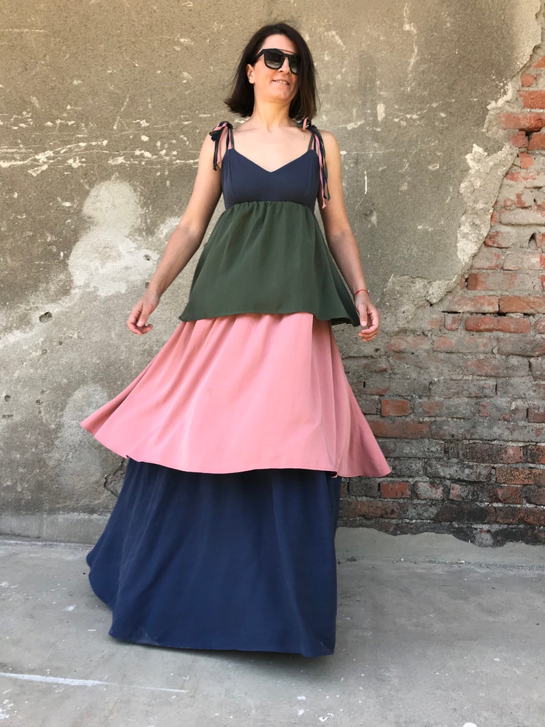May include: A tiered maxi dress with a navy blue, pink, and green color scheme. The dress has a fitted bodice with thin straps and a flowing skirt.