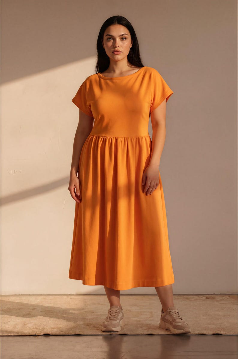 May include: A bright orange midi dress featuring a round neckline, short sleeves, and a gathered waistline that flows into a full, pleated skirt. The garment is paired with neutral-toned athletic sneakers, creating a simple and functional ensemble.