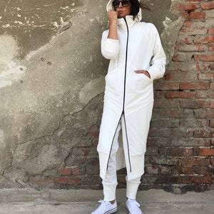 May include: A white hooded sweatshirt with a long zipper and black trim. The sweatshirt is worn with white pants and white sneakers.