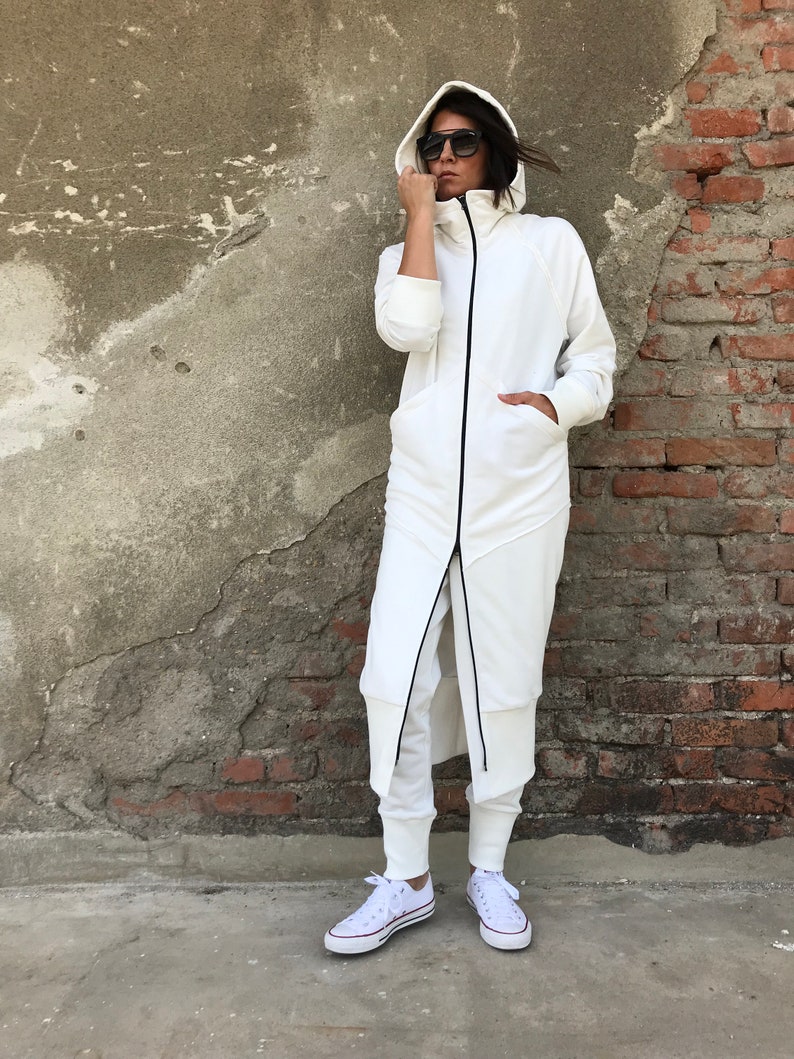 May include: A white hooded sweatshirt with a long zipper and black trim. The sweatshirt is worn with white pants and white sneakers.