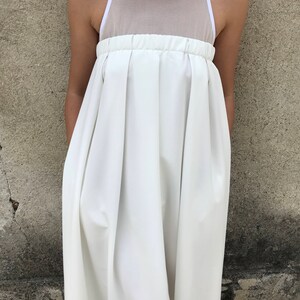 May include: A white sleeveless dress with a mesh panel at the top and a pleated skirt.