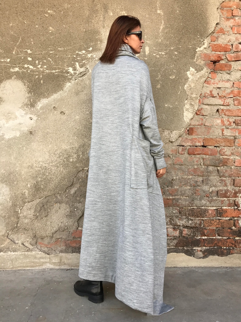 May include: A long, gray, knitted dress with a turtleneck and a large pocket on the side. The dress is made of a soft, comfortable fabric and has a relaxed fit.
