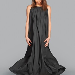 May include: A long, flowing black dress with a high neckline and a full skirt. The dress is made of a soft, draping fabric. The person is wearing pink sneakers.