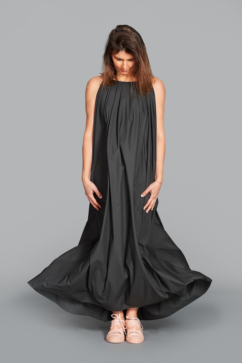 May include: A long, flowing black dress with a high neckline and a full skirt. The dress is made of a soft, draping fabric. The person is wearing pink sneakers.