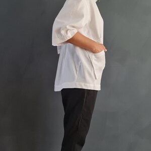 May include: A white collared shirt with a zipper closure and a relaxed fit. The shirt has a slightly puffed sleeve and is paired with black pants and white sneakers.