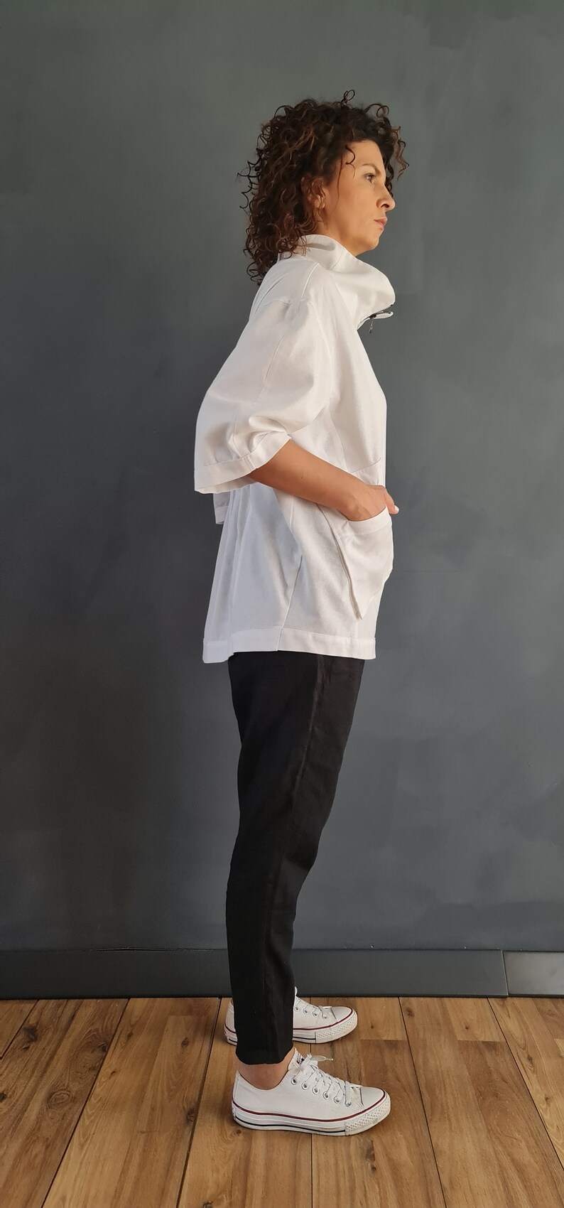 May include: A white collared shirt with a zipper closure and a relaxed fit. The shirt has a slightly puffed sleeve and is paired with black pants and white sneakers.