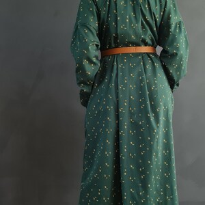 May include: A long green and yellow patterned shirt dress with a brown belt. The dress is worn with matching pants and cream colored sandals.