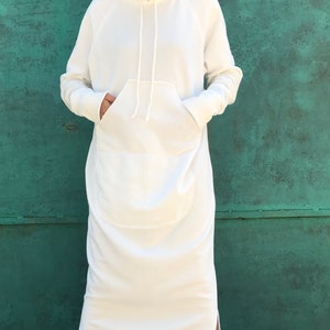 Pu&ograve; includere: Un vestito bianco con cappuccio in felpa, con una grande tasca anteriore e spacchi laterali. Il vestito &egrave; realizzato in un tessuto morbido e confortevole e ha una vestibilit&agrave; rilassata.