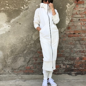 May include: A white hooded sweatshirt dress with a black zipper and pockets. The dress is worn with white sneakers.