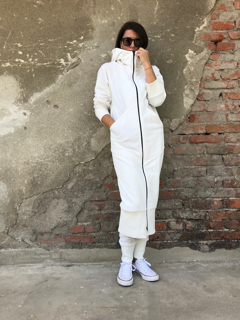 May include: A white hooded sweatshirt dress with a black zipper and pockets. The dress is worn with white sneakers.