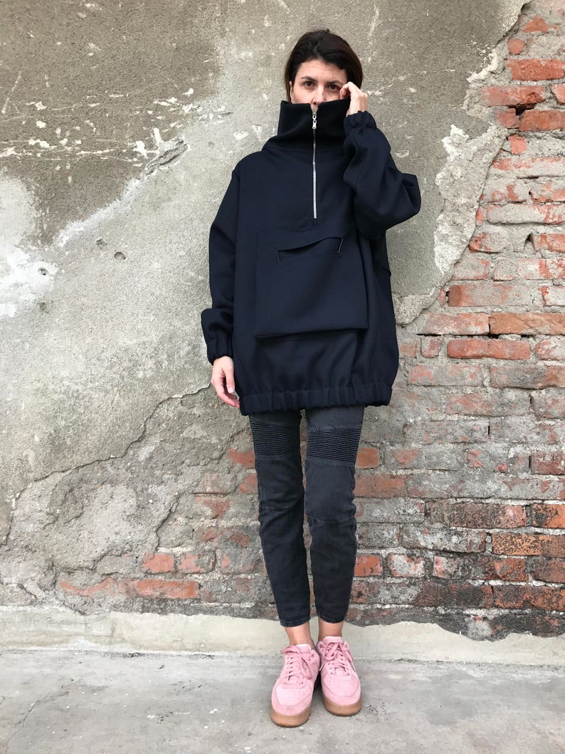 May include: A navy blue oversized sweatshirt with a zipper and a large pocket. The sweatshirt has a high neck and a drawstring at the bottom. The model is wearing black pants and pink sneakers.