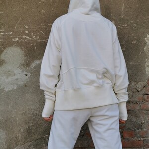 May include: A white hooded sweatshirt with a drawstring hood and long sleeves. The sweatshirt is paired with matching white sweatpants.
