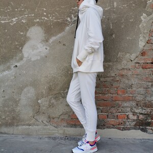 May include: A white hooded sweatshirt and matching sweatpants with a white drawstring. The person is wearing white sneakers with blue and pink accents.