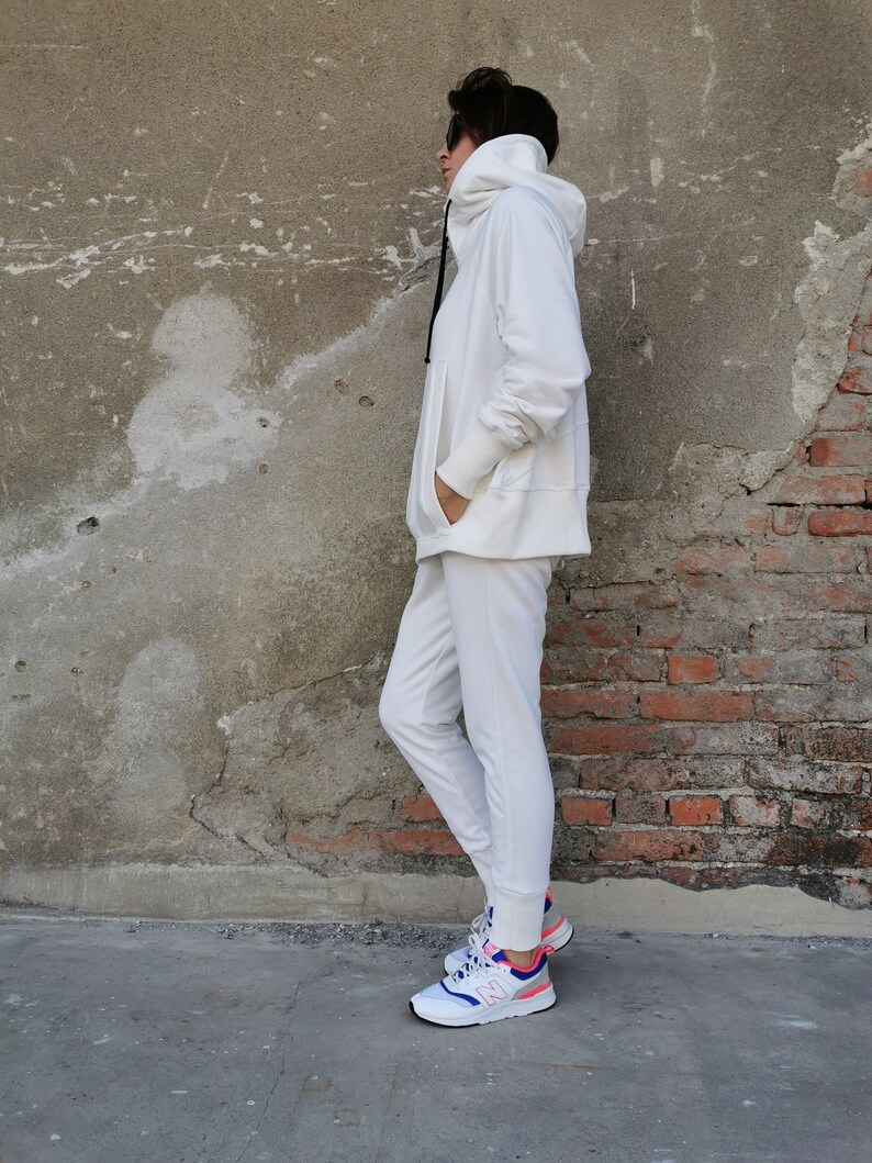 May include: A white hooded sweatshirt and matching sweatpants with a white drawstring. The person is wearing white sneakers with blue and pink accents.