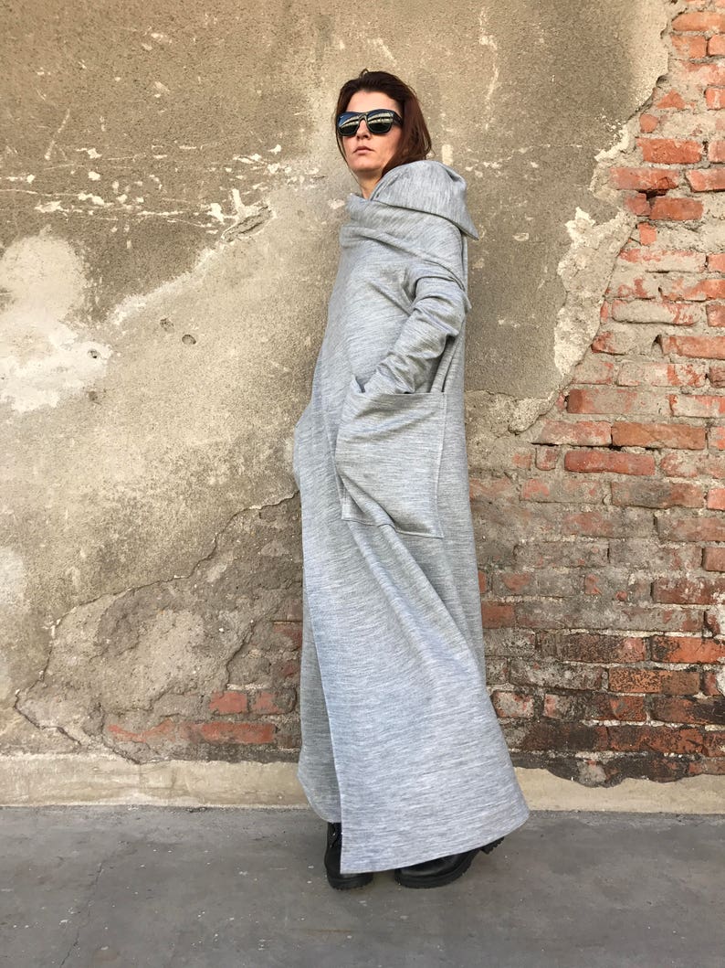 May include: A long, gray hooded dress with a large pocket on the front. The dress is made of a soft, comfortable fabric and has a relaxed fit.