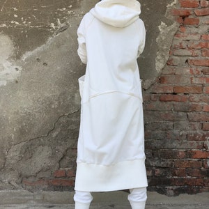 May include: A long white hooded sweatshirt with a relaxed fit and a drawstring hood. The sweatshirt has a large pocket on the front and a ribbed hem and cuffs.