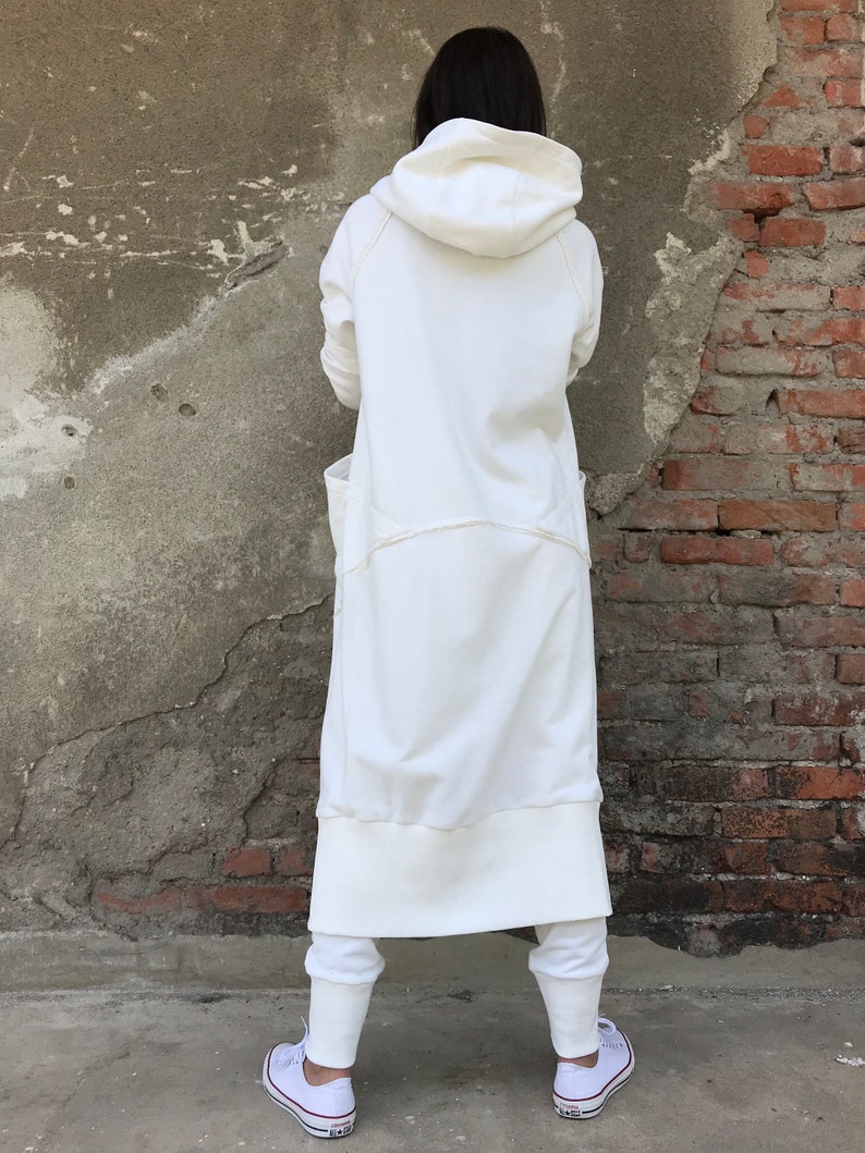 May include: A long white hooded sweatshirt with a relaxed fit and a drawstring hood. The sweatshirt has a large pocket on the front and a ribbed hem and cuffs.