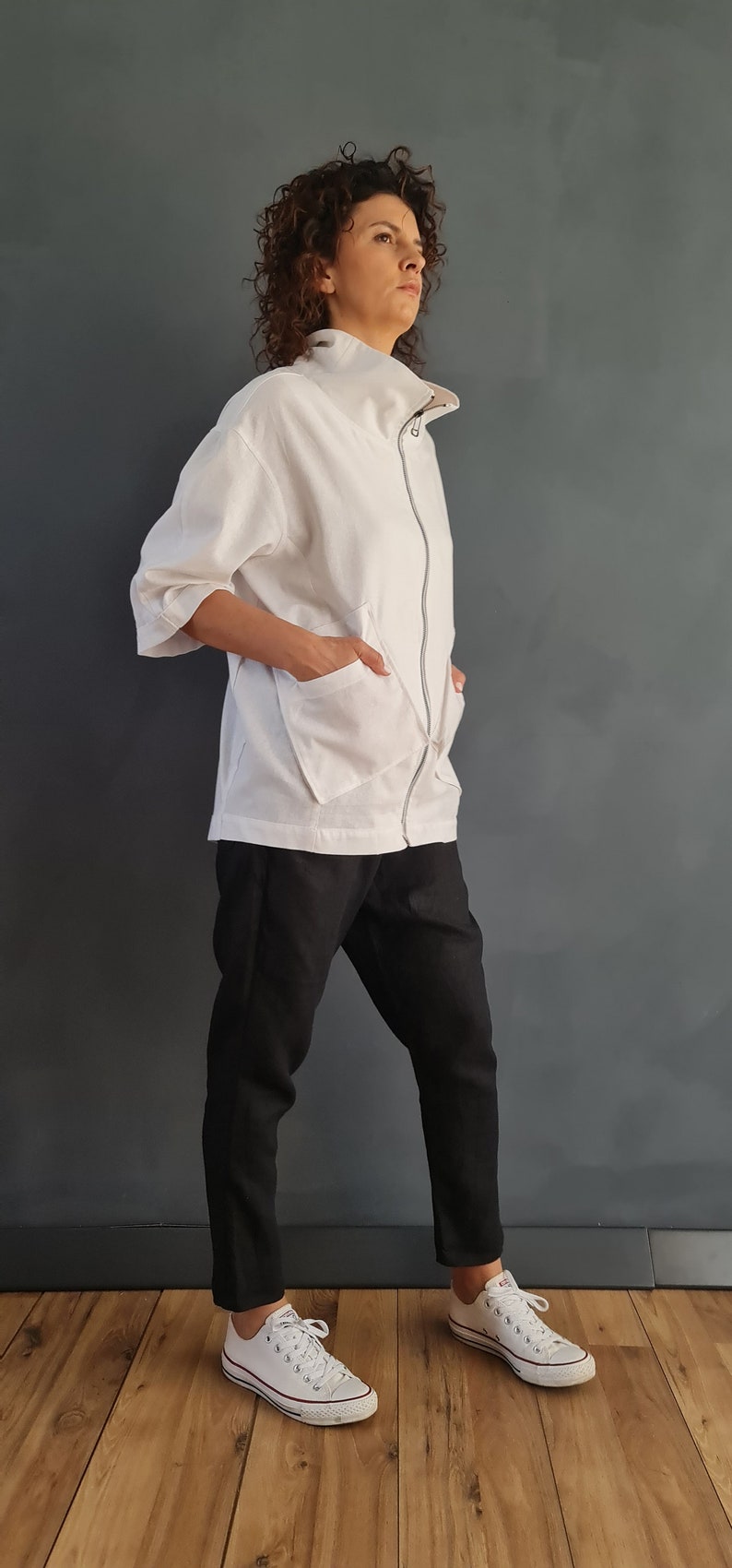 May include: A white zip-up jacket with a high collar and two large pockets. The jacket is worn over black pants and white sneakers.