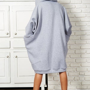May include: A gray oversized hoodie with a hood and large pockets. The hoodie is worn by a person with brown boots.
