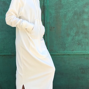 Pu&ograve; includere: Un abito bianco con cappuccio in felpa con uno spacco laterale e una grande tasca sul davanti. L'abito &egrave; realizzato in un tessuto morbido e confortevole e ha una vestibilit&agrave; rilassata.