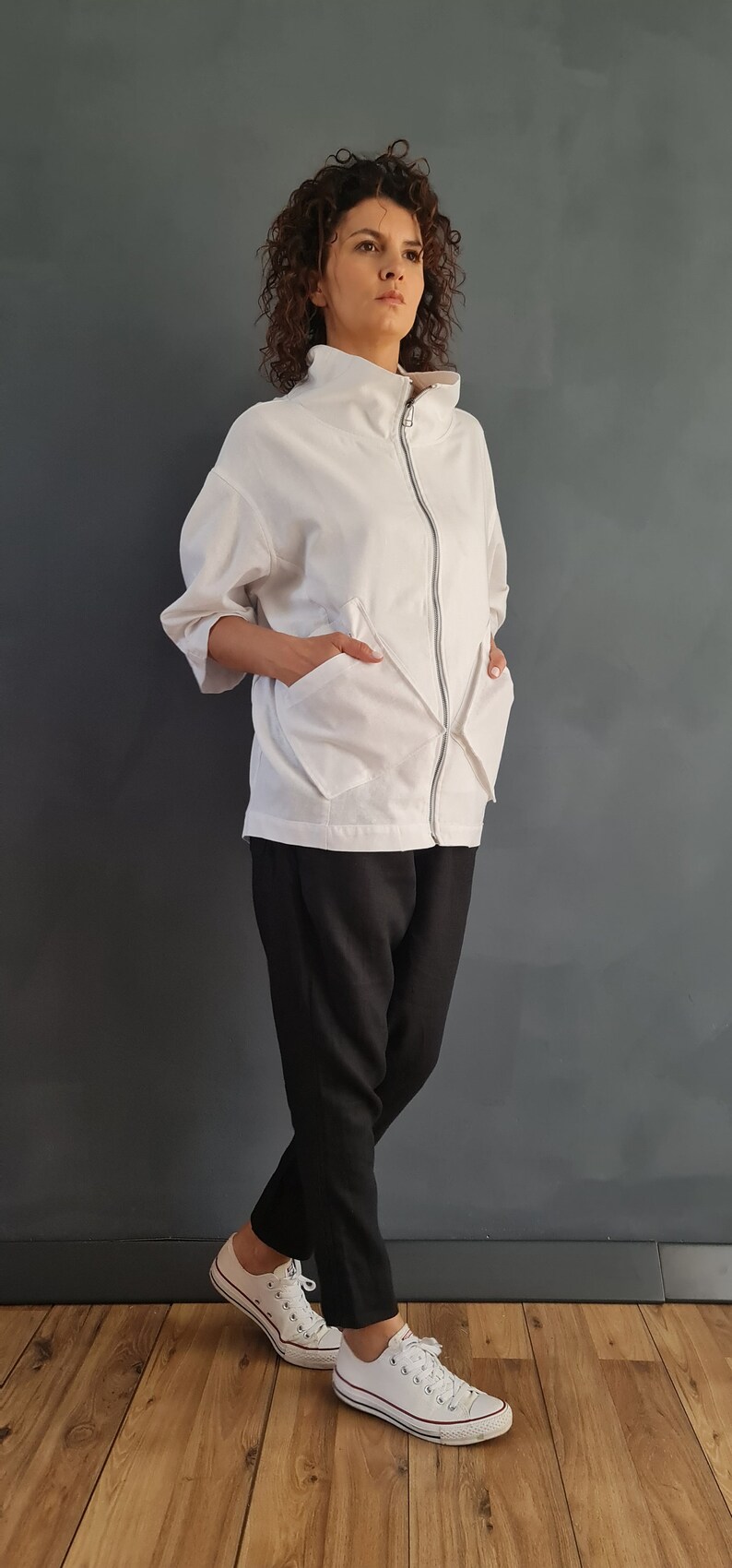 May include: A white zip-up jacket with a high collar and two large pockets. The jacket is worn over black pants and white sneakers.