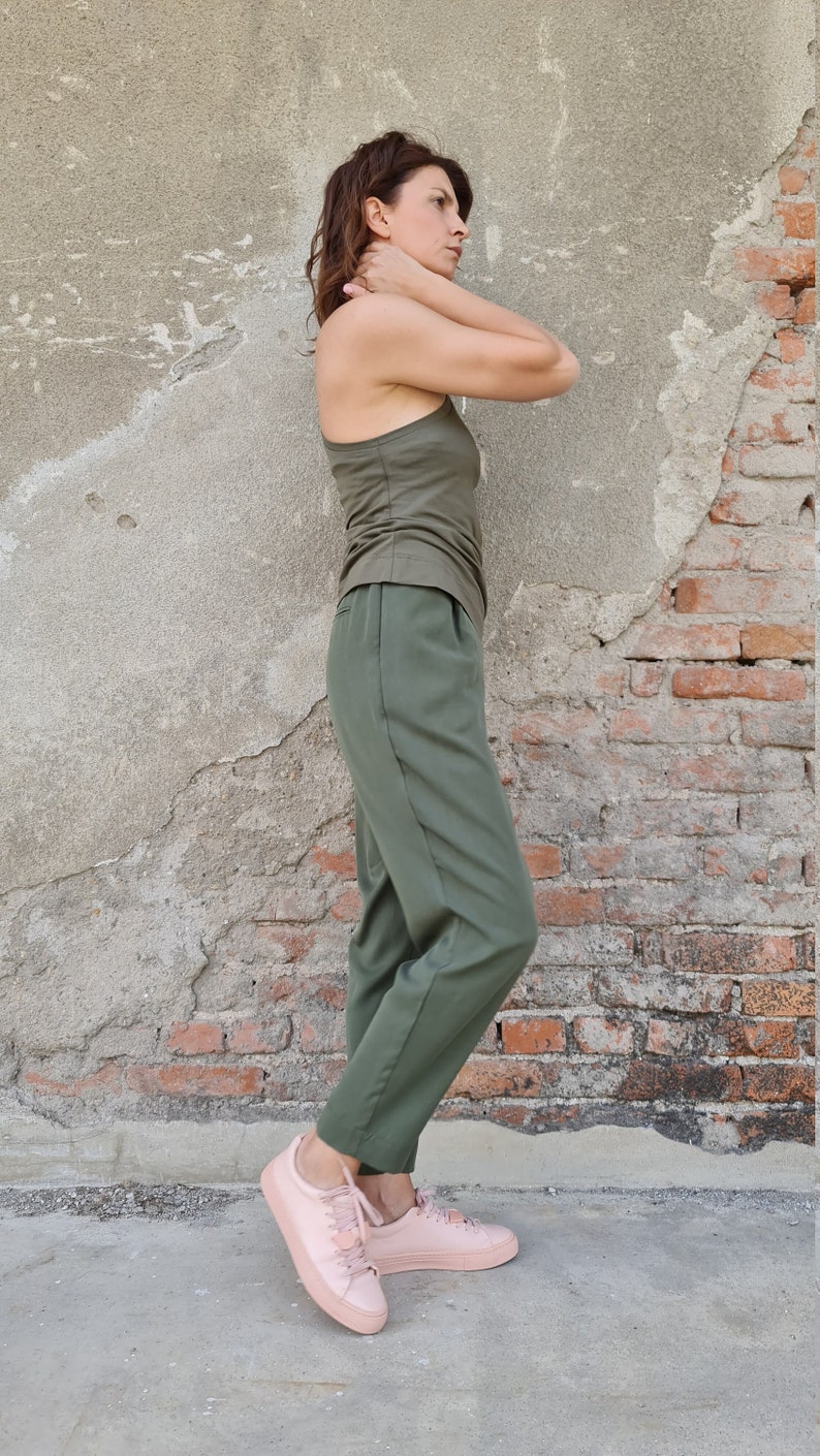 Puede incluir: Una mujer con un top verde sin mangas y pantalones verdes a juego. Lleva zapatillas rosas y est&aacute; de pie frente a una pared de ladrillo.
