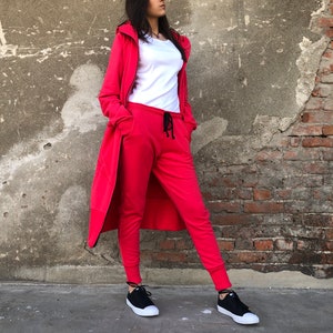 May include: A red hooded sweatshirt and matching sweatpants with a black drawstring. The model is wearing black sneakers.