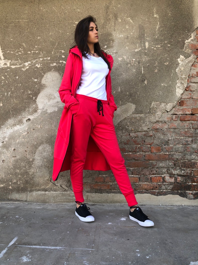 May include: A red hooded sweatshirt and matching sweatpants with a black drawstring. The model is wearing black sneakers.