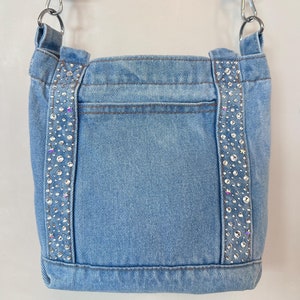 May include: A light blue denim crossbody bag with a silver chain strap and rhinestone embellishments on the front.