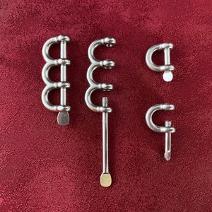 May include: Three silver metal clasps with a rounded shape. The clasps are different sizes and have a small, round, gold-colored knob at the end.