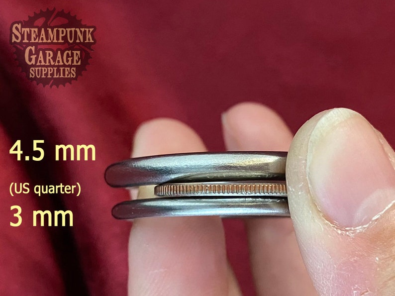 May include: Two metal rings, one 4.5 mm and one 3 mm in diameter, are shown next to a US quarter for size comparison. The rings are silver in color and have a smooth, polished finish.
