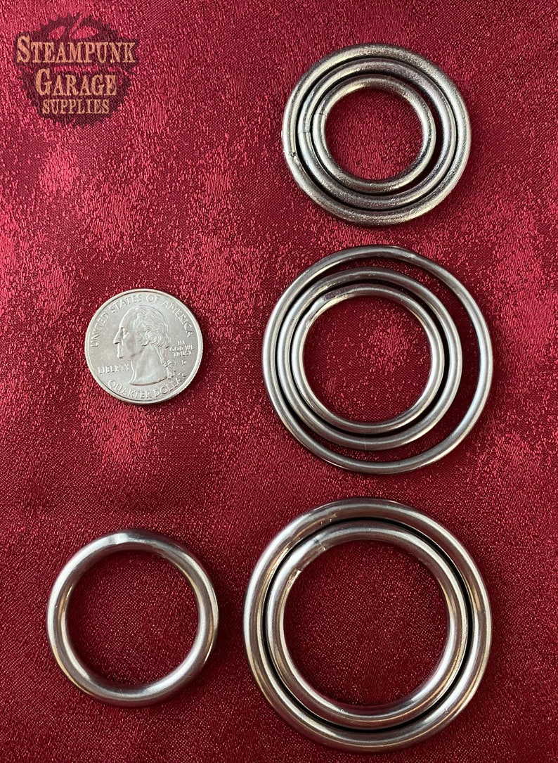 May include: Four sets of metal rings in different sizes, with the smallest ring being about the size of a US quarter. The rings are all silver in color and have a smooth, polished finish. The rings are arranged in a row on a red fabric background.