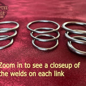 May include: Four sets of interlocking metal rings, stacked on a red surface. The rings are silver in color and have visible welds. The text "STEAMPUNK GARAGE SUPPLIES" is visible in the top left corner of the image.