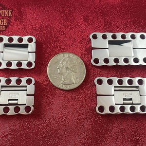 May include: Four silver-toned metal clasps with a hinged design. Each clasp has a rectangular shape with rounded edges and multiple circular holes around the perimeter. The clasps are arranged in two rows of two, with a quarter dollar coin for scale.