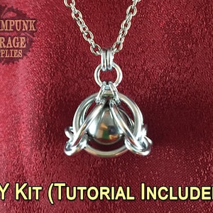 May include: A silver-colored pendant necklace with a spherical center piece, surrounded by a circular design. The necklace hangs on a chain against a red background. Text in the image reads "Steampunk Garage Supplies" and "DIY Kit (Tutorial Included!)".