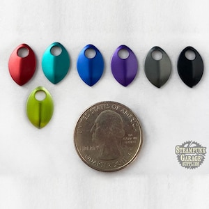 Pode incluir: Sete pingentes de metal em forma de folha com um furo no centro. Os pingentes são de diferentes cores: vermelho, azul-esverdeado, azul, roxo, cinza, preto e verde. Os pingentes são aproximadamente do tamanho de uma moeda de 25 centavos de dólar americano.