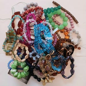 May include: A large collection of assorted loose beads in various shapes, sizes, and colors including bright blue, green, pink, brown, and clear glass. The beads are arranged in multiple strands and clusters, featuring diverse textures and finishes.
