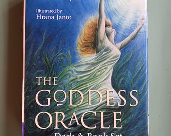 Puede incluir: Un set de caja rectangular titulado The Goddess Oracle Deck & Book Set de Amy Sophia Marashinsky e ilustrado por Hrana Janto. La portada presenta una pintura de una figura con cabello suelto elevándose a través de agua azul hacia la luz.