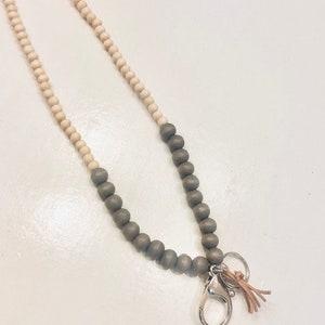 May include: A wooden beaded lanyard with a silver clasp and a brown leather tassel. The beads are a mix of light brown and dark grey.