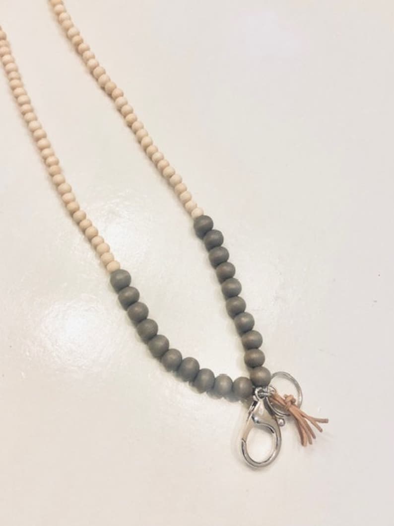 May include: A wooden beaded lanyard with a silver clasp and a brown leather tassel. The beads are a mix of light brown and dark grey.