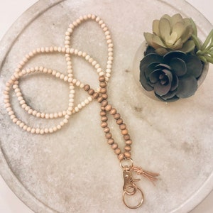 May include: A wooden beaded lanyard with a gold key ring and a tassel. The lanyard is made of two strands of beads, one light brown and one dark brown.
