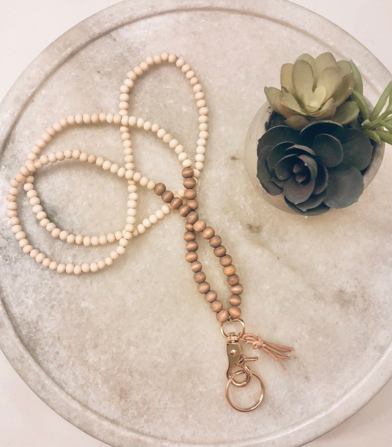 May include: A wooden beaded lanyard with a gold key ring and a tassel. The lanyard is made of two strands of beads, one light brown and one dark brown.