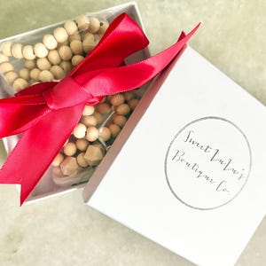 May include: A white gift box with a red ribbon tied around it. The box contains a set of wooden beads. The box has the text "Sweet Lulu's Boutique Co." printed on it.