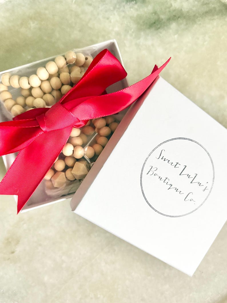 May include: A white gift box with a red ribbon tied around it. The box contains a set of wooden beads. The box has the text "Sweet Lulu's Boutique Co." printed on it.