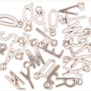 May include: A collection of silver letter charms with jump rings. The letters include A, B, C, D, E, F, G, H, I, J, K, L, M, N, O, P, Q, R, S, T, U, V, W, X, Y, and Z.