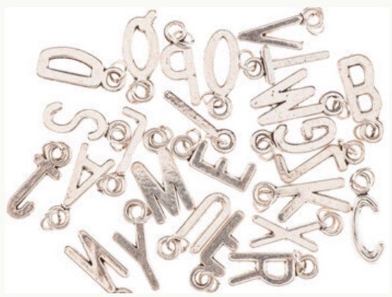 May include: A collection of silver letter charms with jump rings. The letters include A, B, C, D, E, F, G, H, I, J, K, L, M, N, O, P, Q, R, S, T, U, V, W, X, Y, and Z.