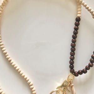 May include: A brown and natural wood beaded lanyard with a gold metal key ring and a brown tassel.